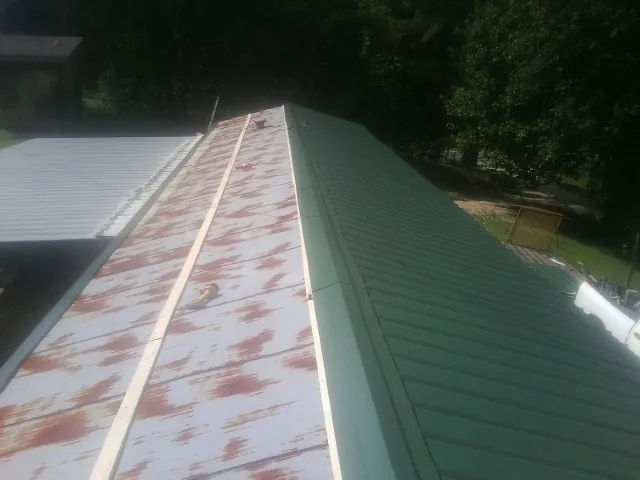 Old rusted panels beside newly installed green metal roofing — Wind Damage Roof Repair by Roofing Brothers in Wingate